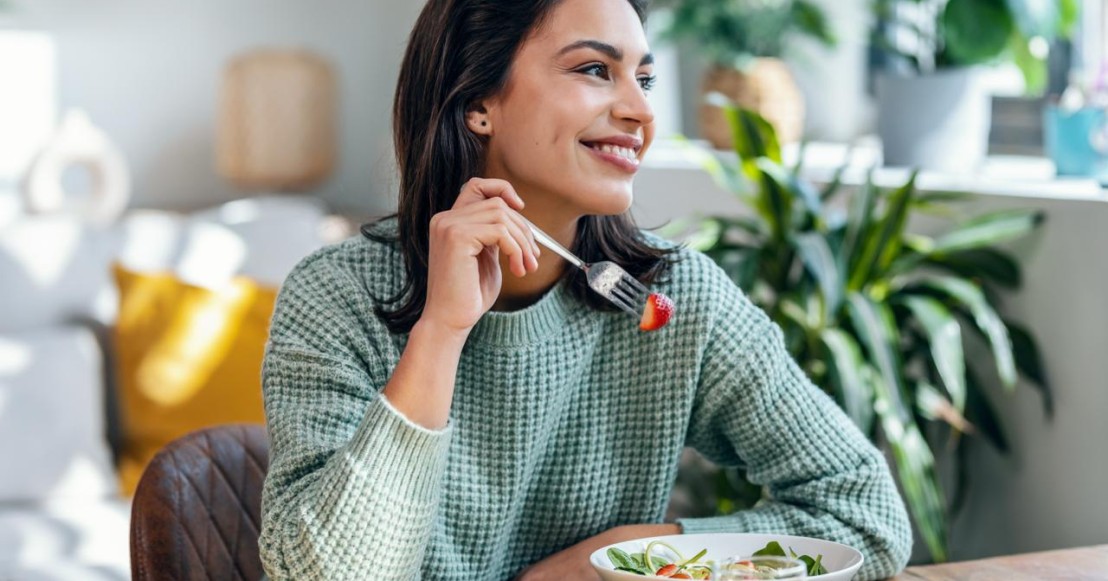 Une femme souriante mange des légumes pour soulager les règles douloureuses