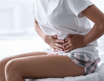 Femme assise sur son lit qui se tient le ventre à cause de ses douleurs de règles
