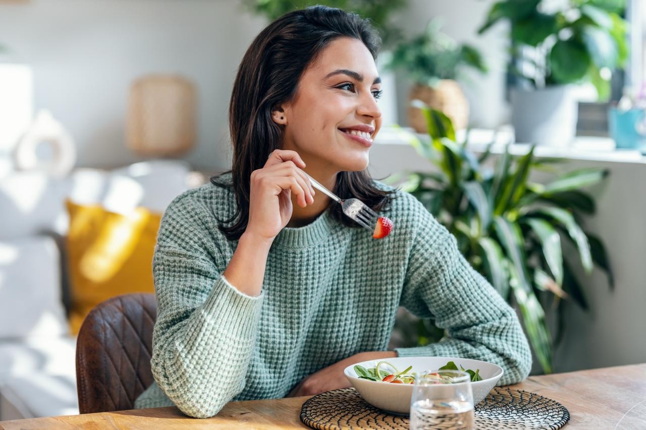 Une femme souriante mange des légumes pour soulager les règles douloureuses